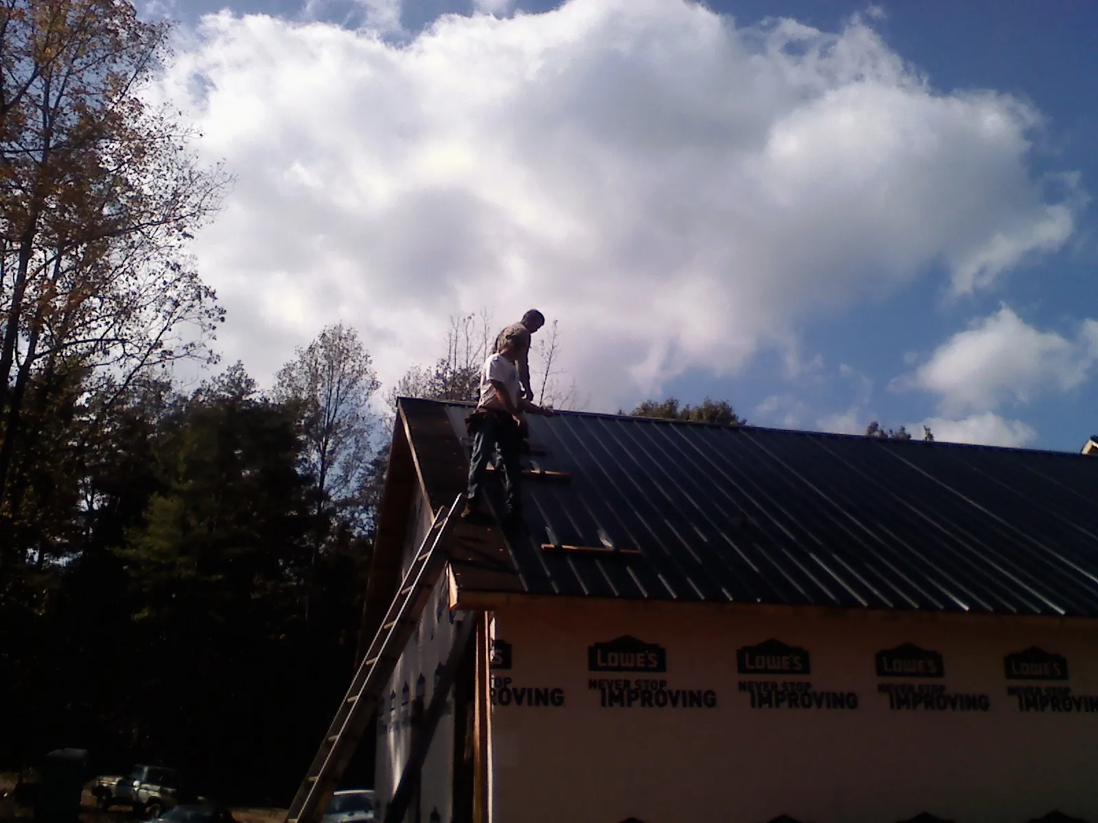 Roofer fastening dark metal panels high against a cloudy sky, from a Roof Inspection job in Hannibal