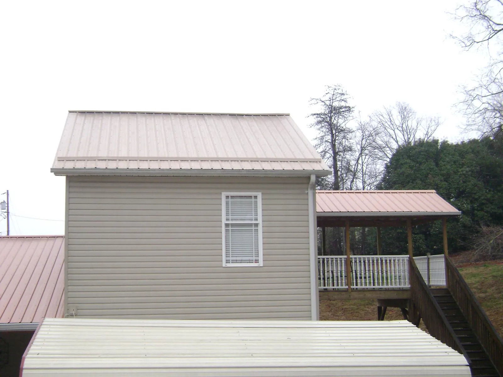 Tan metal roofs on a two story addition and attached porch, from a Roof Replacement job in Hannibal
